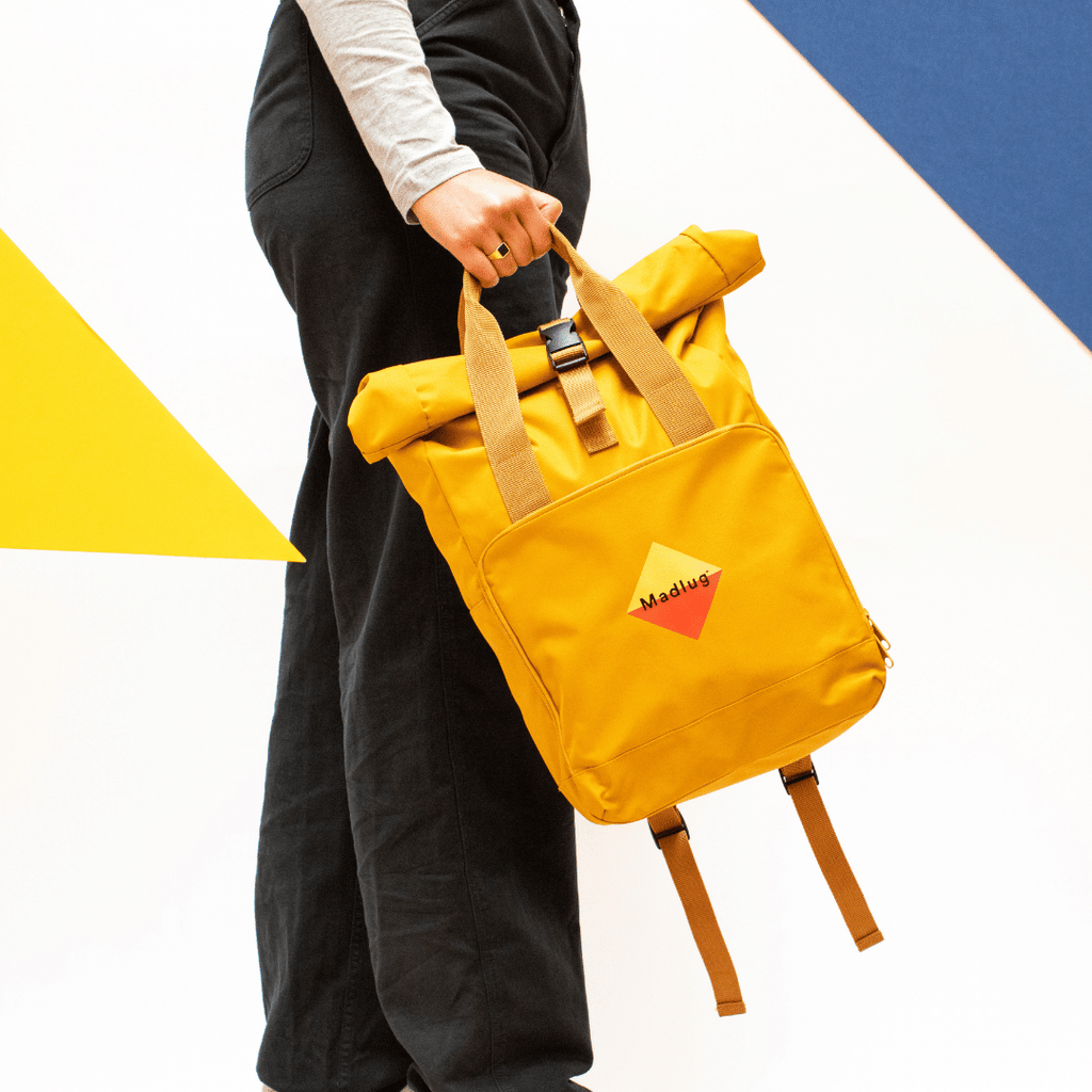 Madlug Roll-Top Backpack in Mustard. Modelled holding bag side profile.